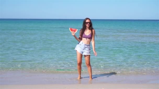 Счастливая девушка веселится на пляже и ест арбуз — стоковое видео