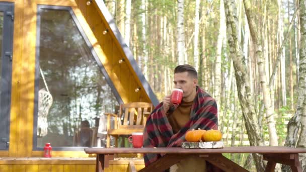 Feliz joven bebiendo café sentado en la mesa de madera al aire libre — Vídeos de Stock
