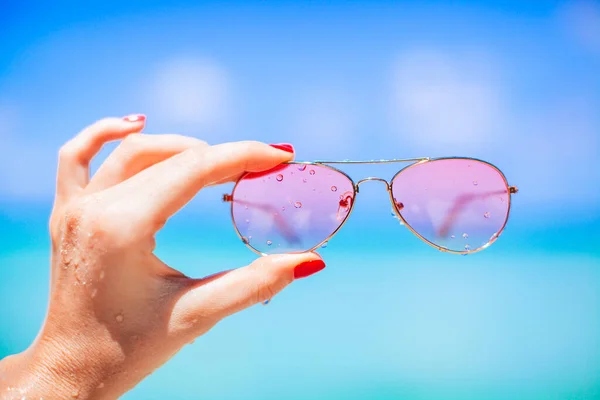 Womans hand holding sunglasses on tropical beach — Stock Photo, Image