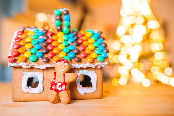 Casa di pan di zenzero di Natale fatta in casa su un tavolo. Luci dell'albero di Natale sullo sfondo — Foto Stock