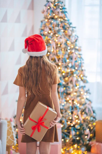 Rückansicht des Kindes hält eine Geschenkbox in der Nähe des Weihnachtsbaums drinnen. — Stockfoto