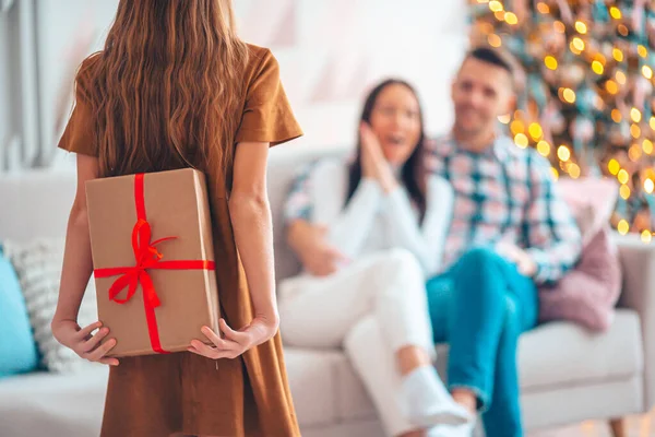 Visão traseira da criança segura uma caixa de presente perto da árvore de Natal dentro de casa. — Fotografia de Stock