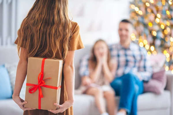 Visão traseira da criança segura uma caixa de presente perto da árvore de Natal dentro de casa. — Fotografia de Stock