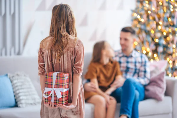 Πίσω όψη του παιδιού κρατά ένα κουτί δώρου κοντά στο χριστουγεννιάτικο δέντρο σε εσωτερικούς χώρους. — Φωτογραφία Αρχείου
