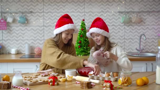 Little girls making Christmas gingerbread house at fireplace in decorated living room. — Stock Video