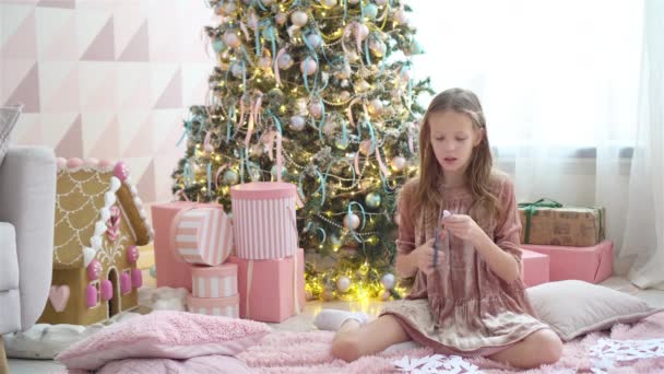 Ağacın yanında oturan ve kağıt kar taneleri yapan sevimli küçük kız. Oda dekore edildi. — Stok video