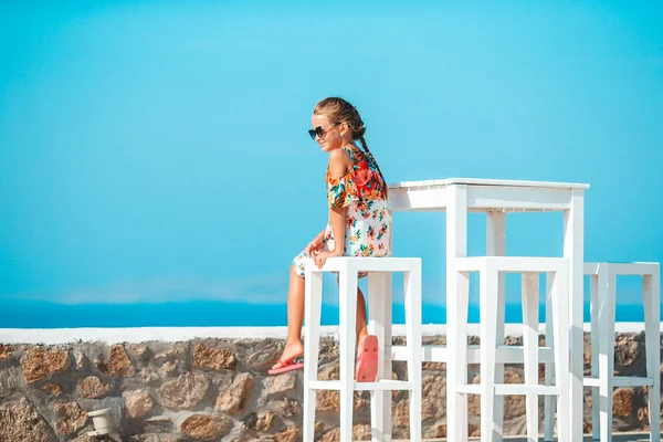 Lunch time. Little girl having breakfast at outdoor cafe with sea view — Stock Photo, Image