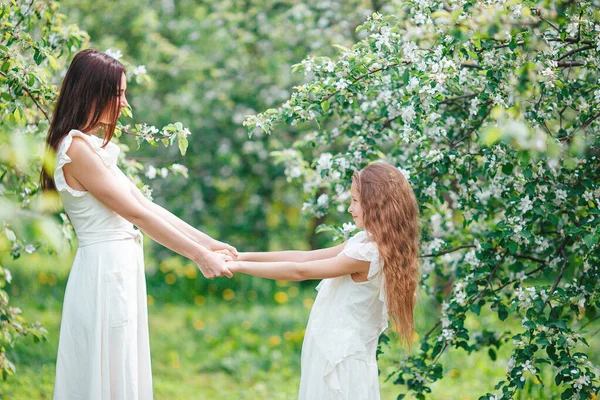Adorable niña con madre joven en el floreciente jardín de cerezos en el hermoso día de primavera —  Fotos de Stock