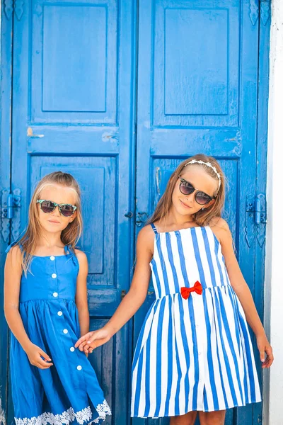 Niñas felices en vestidos en la calle del típico pueblo tradicional griego en la isla de Mykonos, en Grecia —  Fotos de Stock
