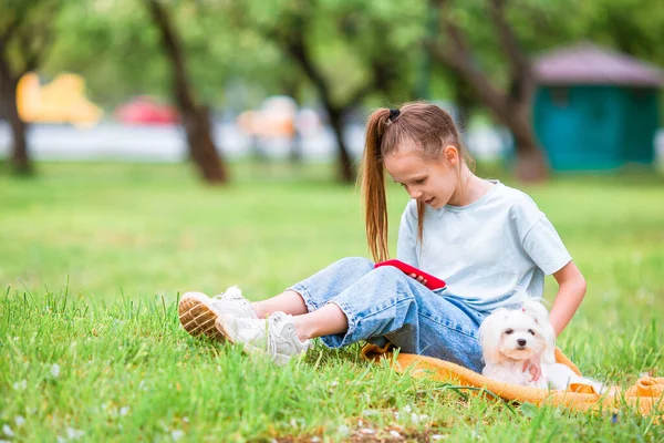 Pequena menina sorridente brincando e abraçando filhote de cachorro no parque — Fotografia de Stock