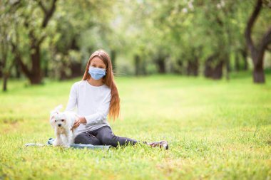 Küçük gülümseyen kız parkta oynaşıyor ve yavru köpeğe sarılıyor.