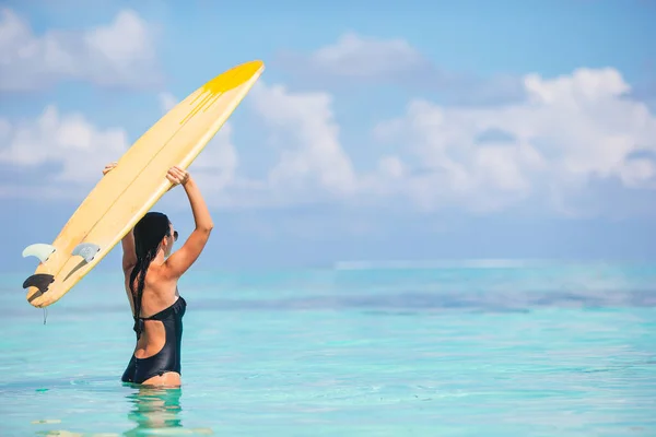 Turkuaz denizde sörf yapmaya hazır güzel bir sörfçü kadın, egzotik bir tatilde ayakta kürek çekiyor. — Stok fotoğraf