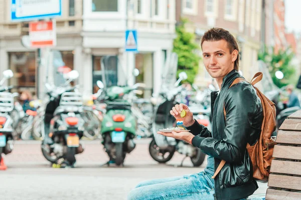 Feliz turista caucásico con arenque fresco con cebolla y bandera de los Países Bajos en Amsterdam. comida holandesa tradicional al aire libre —  Fotos de Stock