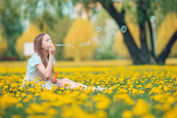 Niña rubia recoger flores en un prado lleno de dientes de león amarillos —  Fotos de Stock