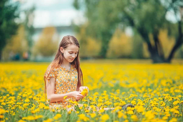 Petite fille blonde cueille des fleurs dans un pré plein de pissenlits jaunes — Photo