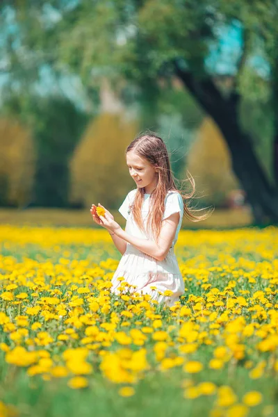 Menina loira pegar flores em um prado cheio de dentes-de-leão amarelos — Fotografia de Stock