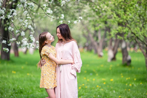 Rozkošná holčička s mladou matkou v kvetoucí třešňové zahradě na krásném jarním dni — Stock fotografie