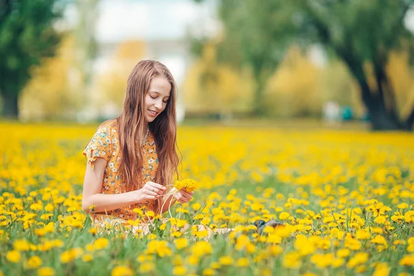 Niña rubia recoger flores en un prado lleno de dientes de león amarillos —  Fotos de Stock