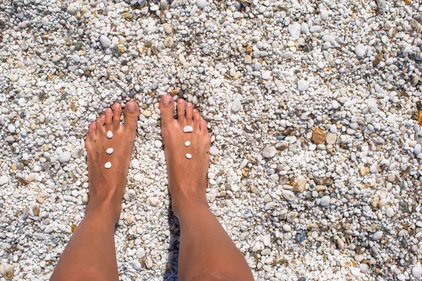 Close up of female legs with pebbles on white sandy beach — Stock Photo, Image