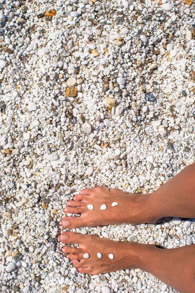 Female legs with pebbles on white sandy beach — Stock Photo, Image