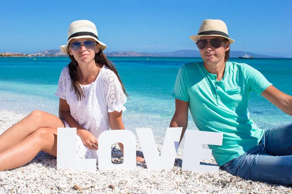 Giovane bella famiglia seduta sulla spiaggia con la parola Amore — Foto Stock