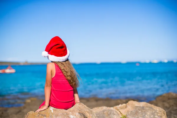 Back view of cute little girl in Santa hat on the beach — Stock Photo, Image