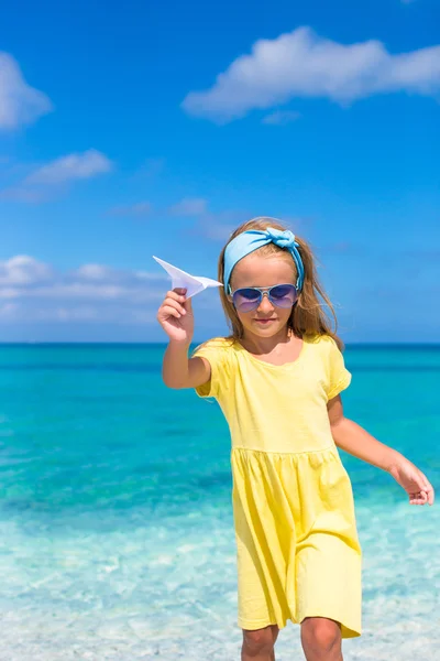 Glückliches kleines Mädchen mit Papierflugzeug in der Hand am weißen Sandstrand — Stockfoto