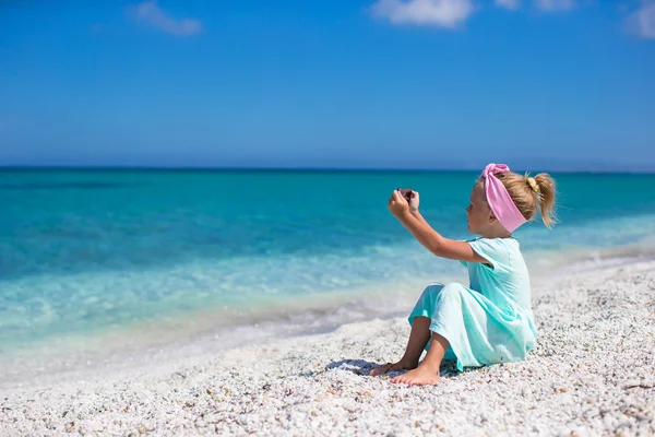 Маленькая милая девочка фотографирует по телефону на тропическом пляже — стоковое фото