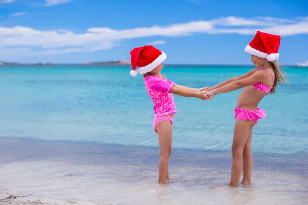 Little cute girls in Christmas hats having fun on exotic beach — Stock Photo, Image