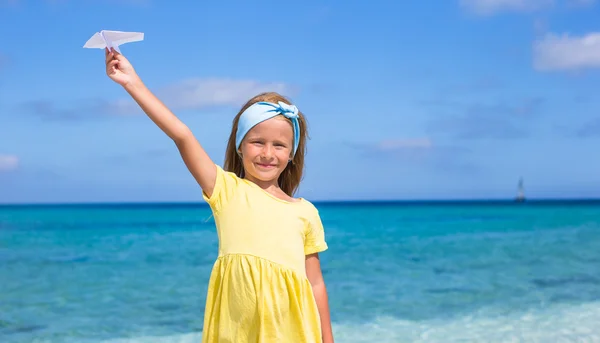 Glückliches kleines Mädchen mit Papierflugzeug in der Hand am weißen Sandstrand — Stockfoto