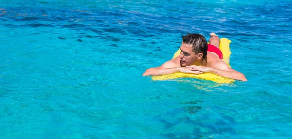 若い男が海で膨脹可能なマットレスでリラックス — ストック写真