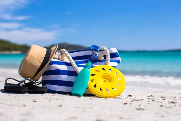 Stripe bag, straw hat, sunblock and frisbee on white sandy tropical beach — Stock Photo, Image