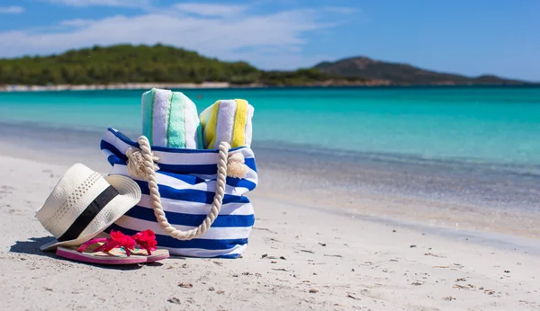 Beach bag, straw hat, flip flops and towel on white tropical beach — Stock Photo, Image