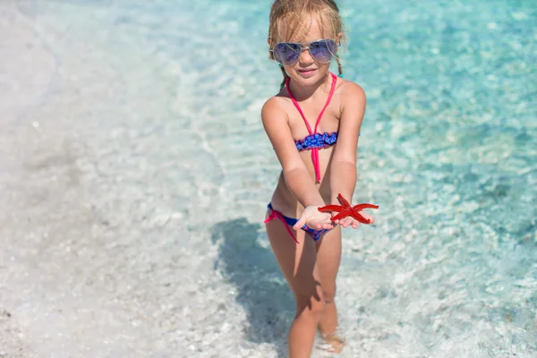 Liten bedårande flicka med sjöstjärnor i händerna på den tropiska stranden — Stockfoto