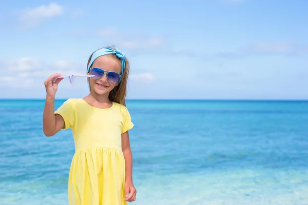 Glad liten flicka med pappersflygplan i händerna på vit sandstrand — Stockfoto