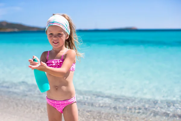 Niña adorable en traje de baño con botella de loción bronceadora — Foto de Stock