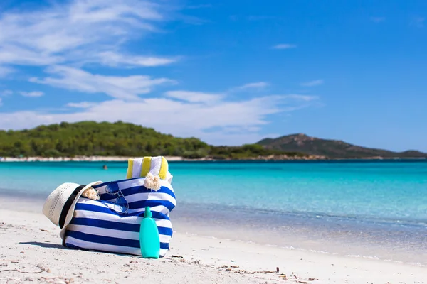 Stripe bag, straw hat, sunblock and towel on white tropical beach — Stock Photo, Image