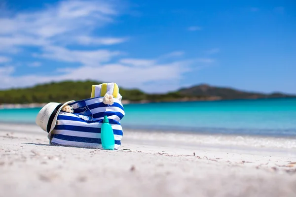 Streifentasche, Strohhut, Sonnencreme und Handtuch am weißen tropischen Strand — Stockfoto