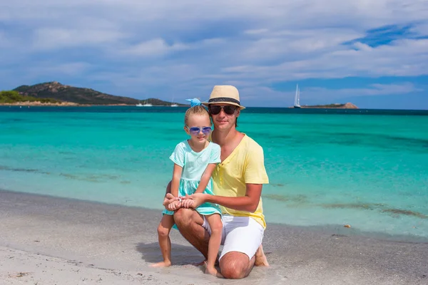 Junger Vater und kleine Tochter sitzen am tropischen weißen Sandstrand — Stockfoto