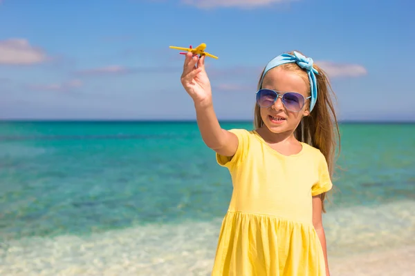 Gelukkig klein meisje met speelgoed vliegtuig in handen op wit zandstrand — Stockfoto