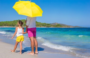 Back view of father and daughter at white beach with yellow umbrella clipart