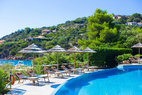 Chaises longues et parasols en bois près de la piscine à débordement dans un complexe de luxe — Photo