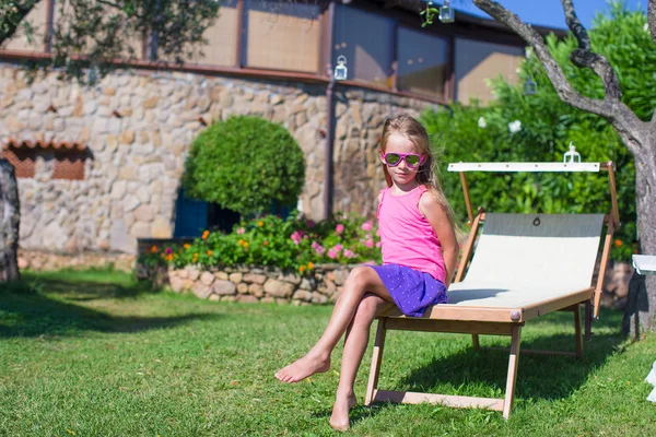 Happy little girl on beach lounger outdoors at exotic resort — Stock Photo, Image