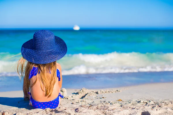 Bakifrån av bedårande liten flicka i stora blå stråhatt på vita stranden — Stockfoto