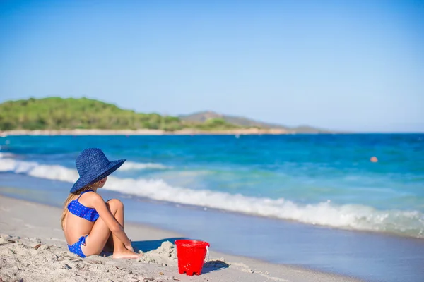 Rear view of adorable little girl in big blue straw hat at white beach — Stock Photo, Image