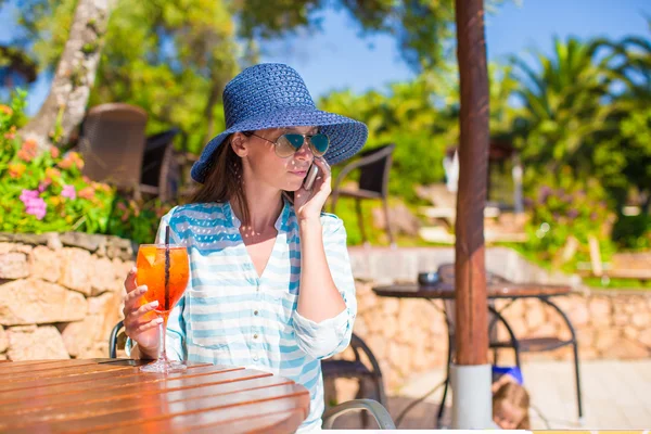 Young woman in hat sitting in tropical cafe near swimming pool — Stock Photo, Image