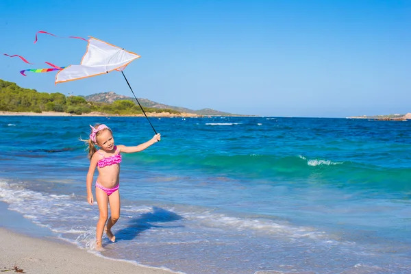 Little happy girl playing with flying kite on tropical beach — Stock Photo, Image