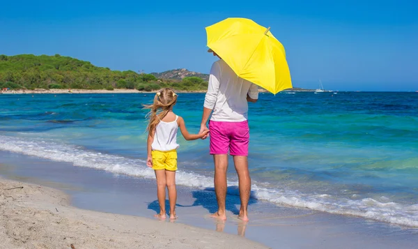 Giovane padre e figlia sulla spiaggia bianca con ombrellone giallo — Foto Stock