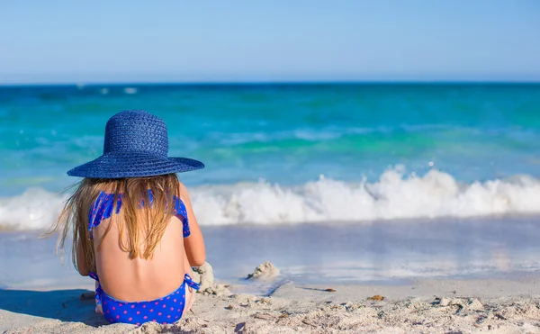 Rear view of adorable little girl in big blue straw hat at white beach — Stock Photo, Image
