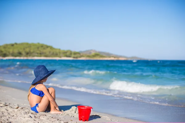 后方的看法的可爱的小女孩，在大的蓝色草帽在洁白的沙滩上 — 图库照片